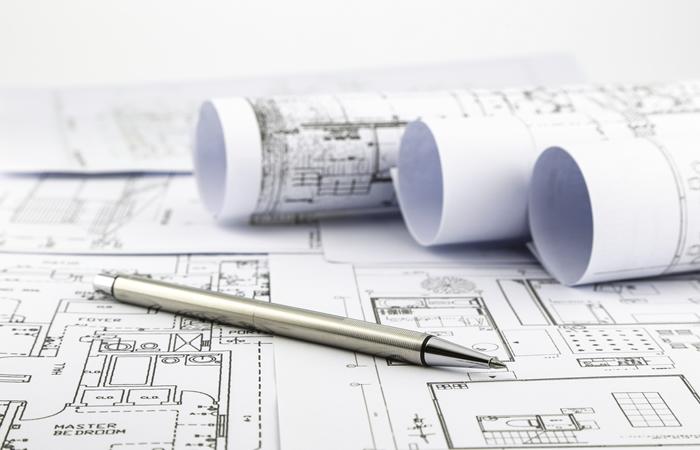 rolled floor plans sitting on top of unrolled floor plan with gold pen